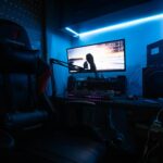 A sleek gaming desk with a monitor, gaming chair, and LED lights creating an immersive environment.