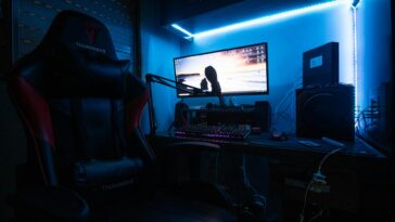 A sleek gaming desk with a monitor, gaming chair, and LED lights creating an immersive environment.