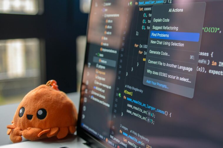 A laptop screen showing a code editor with a cute orange crab plush toy beside it.