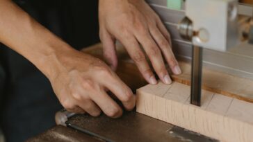 Close-up of hands using a bandsaw on wood in a workshop. Ideal for woodworking themes.