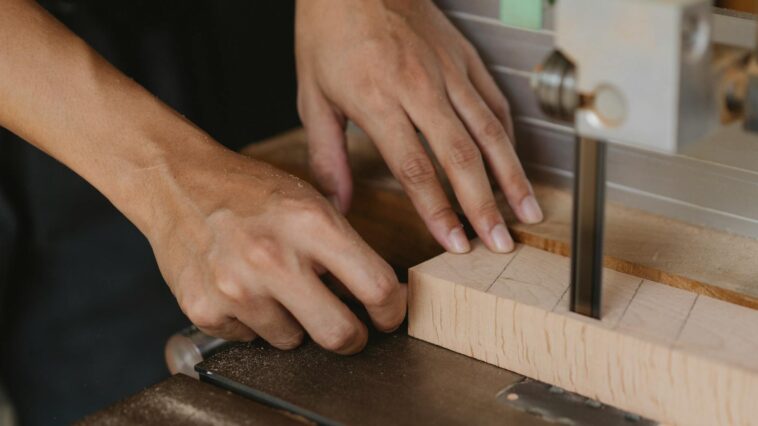 Close-up of hands using a bandsaw on wood in a workshop. Ideal for woodworking themes.