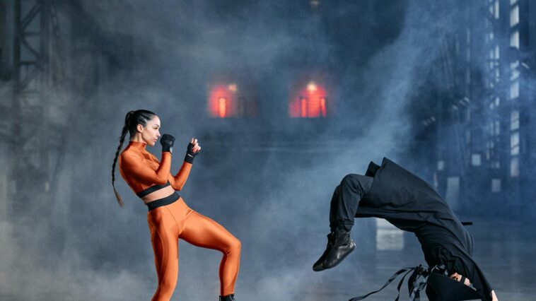 Two cosplayers in martial arts poses amidst smoke, embodying game characters in action.