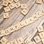 Wooden letter tiles forming the word 'COMPLIANCE' on a rustic wooden background.