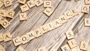 Wooden letter tiles forming the word 'COMPLIANCE' on a rustic wooden background.
