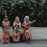 Three musicians in traditional attire performing with guitar and flute outdoors.