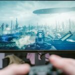 A person playing a video game on a high-resolution monitor, showcasing a war-themed landscape.
