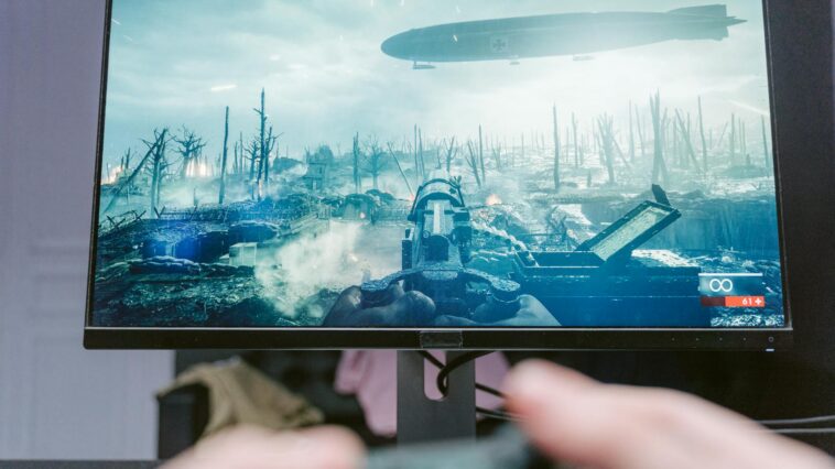 A person playing a video game on a high-resolution monitor, showcasing a war-themed landscape.
