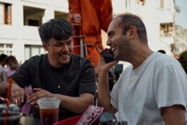 Two men smiling and chatting over drinks at an outdoor café.