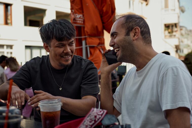 Two men smiling and chatting over drinks at an outdoor café.
