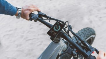 A modern electric bicycle handlebar with a touch screen display, featuring riding statistics on a sandy outdoor surface.