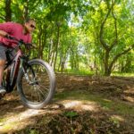 An adult man enjoying a ride on an electric mountain bike through a lush forest trail in summer.