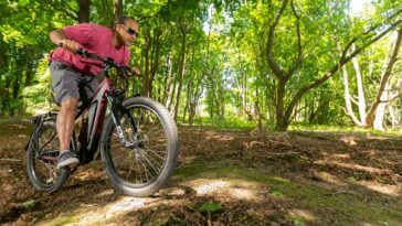 An adult man enjoying a ride on an electric mountain bike through a lush forest trail in summer.