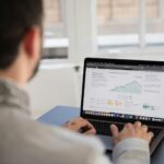 A person working on a laptop analyzing financial data in a bright indoor setting.