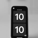 Close-up of a smartphone showing a digital clock set to 10:10 on a blurred background.