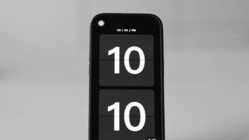 Close-up of a smartphone showing a digital clock set to 10:10 on a blurred background.