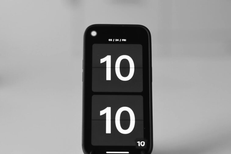 Close-up of a smartphone showing a digital clock set to 10:10 on a blurred background.