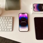 A sleek workspace setup featuring an iPhone with colorful display beside a keyboard and plant.