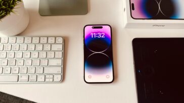 A sleek workspace setup featuring an iPhone with colorful display beside a keyboard and plant.