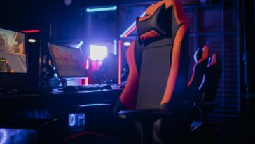 Modern gaming setup featuring a sleek chair and powerful PCs under neon lights.