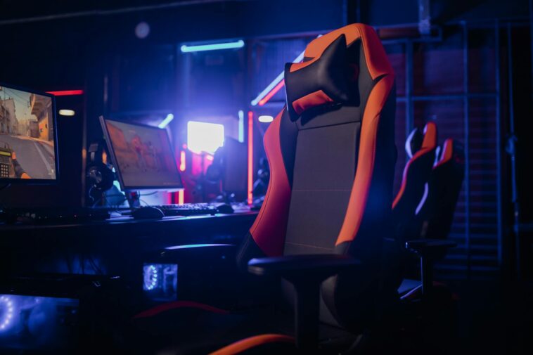 Modern gaming setup featuring a sleek chair and powerful PCs under neon lights.