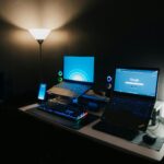 A sleek gaming desk with two laptops, RGB keyboard, and ambient lighting for a modern tech setup.