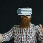 Bearded man in plaid shirt using virtual reality headset indoors, immersed in VR experience.