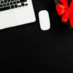 Flat lay of laptop and gift box with red bow on black background. Ideal for online shopping or gift themes.