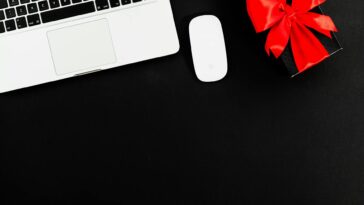 Flat lay of laptop and gift box with red bow on black background. Ideal for online shopping or gift themes.