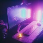 A stylish gaming desk featuring neon lights, keyboard, and monitor in a dark room.