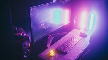 A stylish gaming desk featuring neon lights, keyboard, and monitor in a dark room.