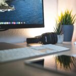 A minimalistic desk setup featuring a monitor, headphones, keyboard, and green plants for a tech-savvy workspace.