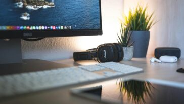 A minimalistic desk setup featuring a monitor, headphones, keyboard, and green plants for a tech-savvy workspace.