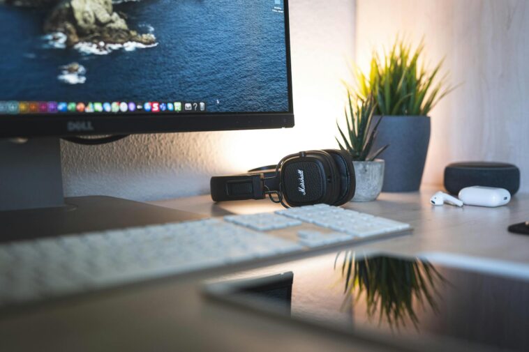 A minimalistic desk setup featuring a monitor, headphones, keyboard, and green plants for a tech-savvy workspace.