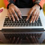 A person typing on a laptop with a Python programming book visible, capturing technology and learning.