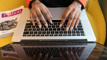A person typing on a laptop with a Python programming book visible, capturing technology and learning.