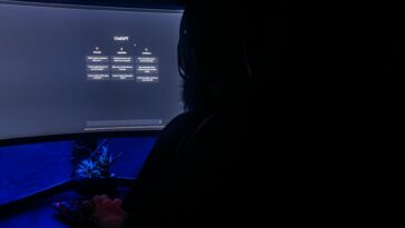 Silhouette of a person using ChatGPT on a computer screen in a dark room, highlighting digital interaction.