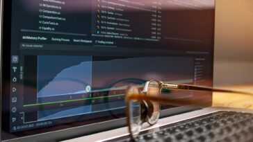 Laptop screen displaying code and performance graphs with eyeglasses resting on the keyboard.