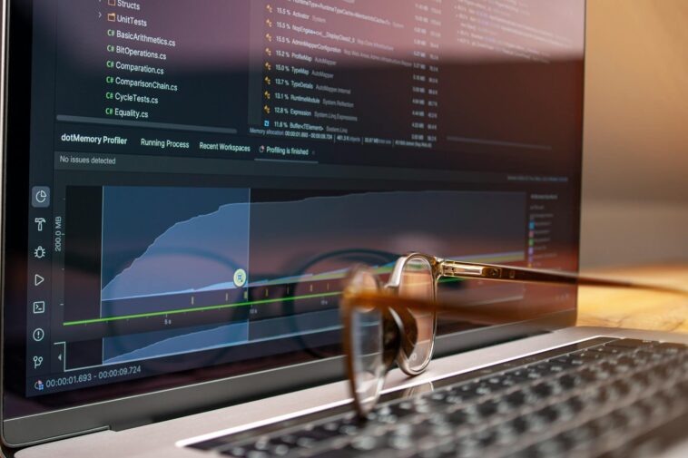 Laptop screen displaying code and performance graphs with eyeglasses resting on the keyboard.