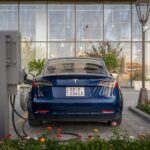 Rear view of a blue Tesla electric vehicle charging at a modern outdoor station.