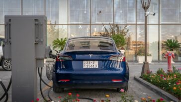 Rear view of a blue Tesla electric vehicle charging at a modern outdoor station.
