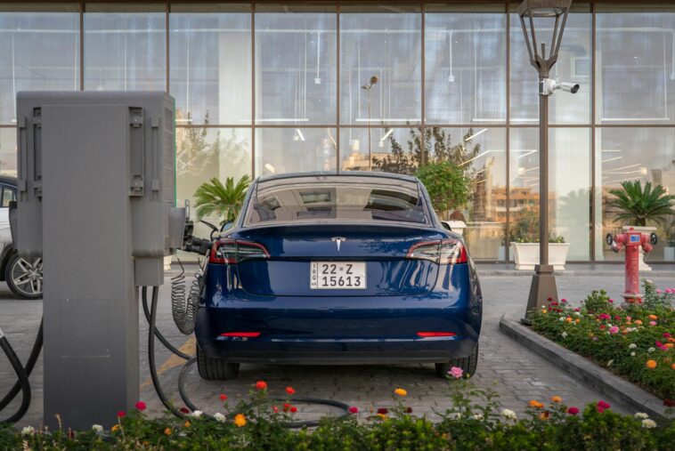 Rear view of a blue Tesla electric vehicle charging at a modern outdoor station.