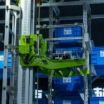 High-tech automated warehouse system featuring a green robotic arm handling blue storage crates.