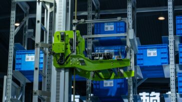 High-tech automated warehouse system featuring a green robotic arm handling blue storage crates.