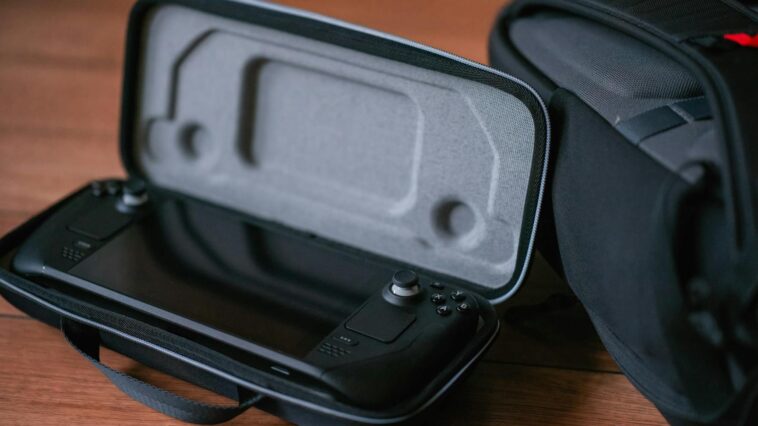 A close-up of a portable gaming device in a protective case next to a bag on a wooden floor.