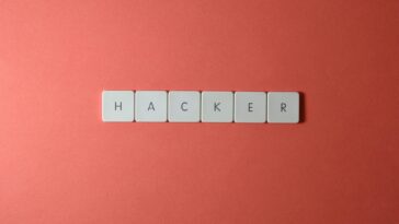 Close-up of the word 'HACKER' made with letter tiles on a red background, emphasizing cybersecurity.