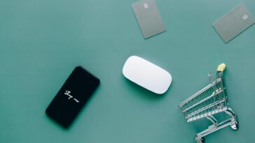 Flat lay of smartphone, cards, and shopping cart on green. Perfect for e-commerce and online shopping themes.