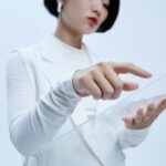 Woman touches transparent interface in a modern, futuristic setting.