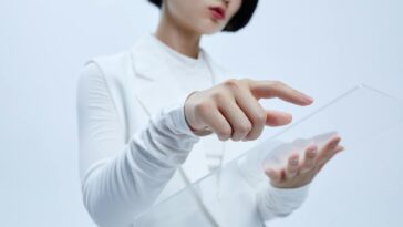 Woman touches transparent interface in a modern, futuristic setting.