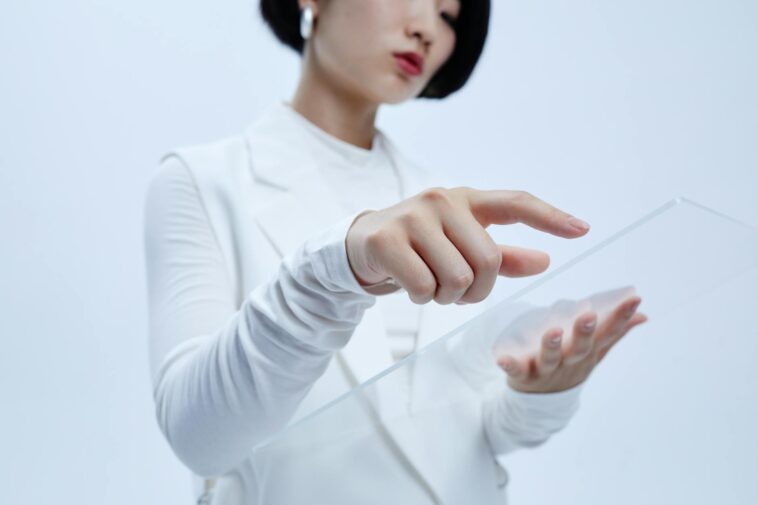 Woman touches transparent interface in a modern, futuristic setting.