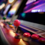 Close-up of a colorful vintage arcade machine with glowing joysticks and buttons in a dimly lit game room.